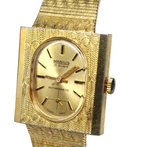 Puede incluir: Un reloj de pulsera dorado con una caja cuadrada y una esfera de forma ovalada. La esfera tiene marcadores de hora romanos negros, agujas negras y el texto "MANIUS 17 RUBIS" y "ANTIMAGNETIC".