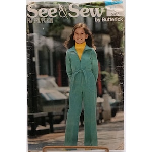 Peut inclure: Une pochette de patron de couture See & Sew by Butterick 5787 présentant une combinaison à manches longues bleu sarcelle avec fermeture éclair frontale, ceinture à nouer et jambes larges, portée sur un col roulé jaune.