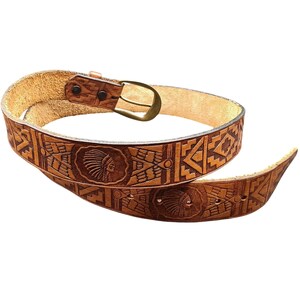 May include: A brown leather belt with a decorative Native American design. The belt features an embossed pattern with geometric shapes and two medallions with a Native American profile. The buckle is brass-colored.