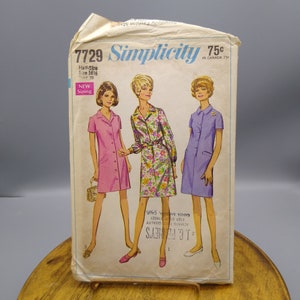 May include: Vintage Simplicity sewing pattern number 7729 for a dress. The pattern is for half sizes 16 1/2 and bust 39. The pattern shows three women wearing different versions of the dress. The dress is a simple, collared, short-sleeved dress with a button-up front. The dress is shown in pink, floral print, and purple.