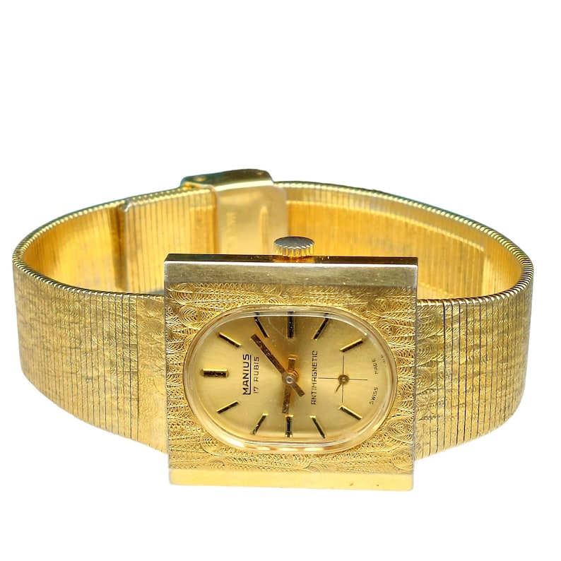 Puede incluir: Un reloj de pulsera dorado con una esfera cuadrada y una correa de metal dorado. La esfera del reloj tiene una esfera dorada con agujas negras y marcadores negros. La esfera del reloj tambi&eacute;n tiene el texto "MANIUS 17 RUBIS ANTI-MAGNETIC" impreso en ella.