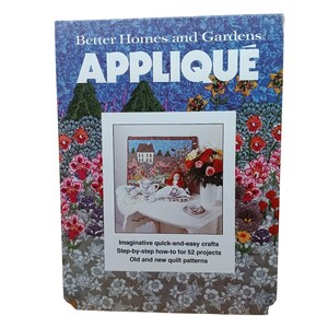 May include: A book titled "Better Homes and Gardens Applique" with a colourful floral design on the cover. The book features a photo of a quilt with a house and flowers. The text on the cover reads "Imaginative quick-and-easy crafts, Step-by-step how-to for 52 projects, Old and new quilt patterns."