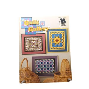 Puede incluir: Libro de patrones de Quilt Gallery con una portada que presenta tres diseños de punto de cruz enmarcados. Los diseños son un girasol, un patrón geométrico y un patrón floral. El libro es publicado por Annie's Attic.