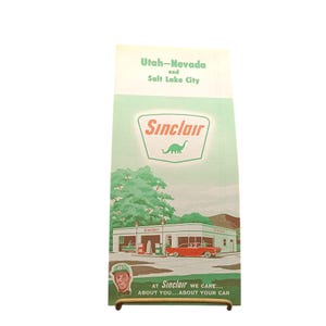 Può includere: Annuncio pubblicitario vintage della stazione di servizio Sinclair con un'auto rossa e un logo di dinosauro verde. L'annuncio è per Utah-Nevada e Salt Lake City. Il testo recita "AT Sinclair WE CARE... ABOUT YOU... ABOUT YOUR CAR."