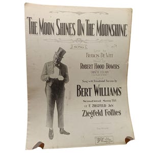 May include: Vintage sheet music titled "The Moon Shines on the Moonshine" featuring a black and white illustration of a man in formal attire. The sheet music includes the names of the lyricist, composer, and performer, Bert Williams.