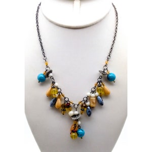 May include: A silver chain necklace with a variety of colorful beads, including turquoise, yellow, and brown. The necklace has a dangling charm with a turquoise bead at the bottom.