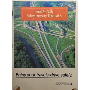 May include: A Rand McNally Safety Interstate Road Atlas, showcasing a detailed aerial view of motorway junctions. The cover has text in a red rectangle, with the slogan "Enjoy your travels-drive safely."