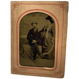 Antica fotografia di ferrotipia in cornice di carta, marito e moglie ferrotype ritratto in cappelli e raffinatezza, coppia uomo e donna vintage