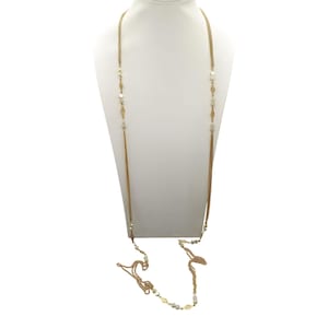 Op de afbeelding: Een lange goudkleurige ketting met een delicaat kettingontwerp. De ketting heeft afwisselende secties van kleine, ronde en ruitvormige accenten. De ketting wordt gepresenteerd op een witte mannequin.