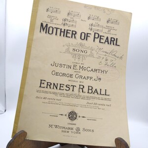 Puede incluir: Partitura antigua de la canción "Mother of Pearl", con notas musicales y letras. La portada muestra los nombres de los letristas, el compositor y la editorial, M. Witmark & Sons, Nueva York. El papel está amarillento.