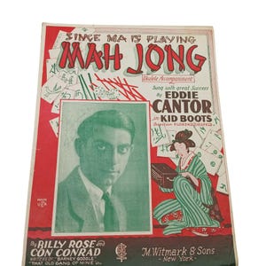 Può includere: Copertina di spartito vintage per "Mah Jong" con Eddie Cantor. La copertina ha uno sfondo rosso e bianco con il titolo a lettere grandi. Un ritratto di Cantor è a sinistra e un'illustrazione di una donna in kimono a destra.
