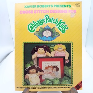 May include: A vintage cross-stitch pattern book titled "Xavier Roberts Presents Cross Stitch Designs For Cabbage Patch Kids." The cover is yellow with the Cabbage Patch Kids logo and images of dolls. The book includes the text "All Babies are Special."