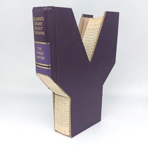 May include: A purple bookend shaped like the letter Y. The bookend is made from a book with the title "The Street Lawyer" and the words "Reader's Digest Select Editions" on the spine.