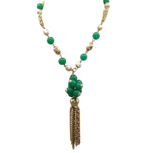 Puede incluir: Un collar de cadena dorada con cuentas verdes y blancas y un borla dorada. El collar tiene un racimo de cuentas verdes en la parte inferior.