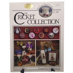 May include: A craft pattern booklet titled The Cricket Collection No. 68 Buttons & Bows by Vicki Hastings. The cover features various cross-stitch designs including small circular motifs, teddy bears with bows, and a bear holding a wooden paddle.
