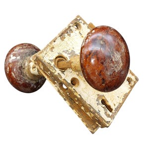 May include: Antique door knob set with a distressed, peeling white finish and brown wooden knobs. The hardware has a vintage aesthetic, showcasing signs of wear and age.