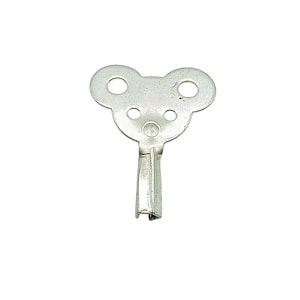 Puede incluir: Una llave de reloj plateada con una cabeza en forma de oso, con tres agujeros circulares. La llave tiene un vástago rectangular y está diseñada para dar cuerda a relojes mecánicos. La llave es de metal y está sobre un fondo blanco.