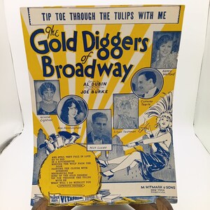 Puede incluir: Una portada de partitura vintage amarilla y azul para el musical "The Gold Diggers of Broadway". La portada presenta un elenco de actores y actrices, incluyendo a Winnie Lightner, Ann Pennington, Conway Tearle y Nancy Welford. La letra es de Al Dubin y la música de Joe Burke. La partitura es publicada por M. Witmark & Sons.