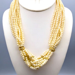 Puede incluir: Un collar de perlas de múltiples hilos con detalles dorados. El collar está hecho de pequeñas perlas blancas y tiene un diseño anudado.