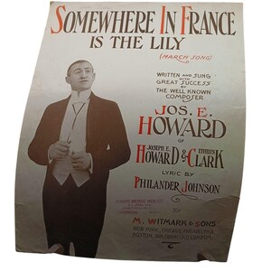 May include: A vintage sheet music cover featuring a man in a tuxedo, with the title "Somewhere in France is the Lily (March Song)". The music was written and sung by Jos. E. Howard of Howard & Clark, with lyrics by Philander Johnson. The cover is printed on a light brown paper with a faded, vintage look.