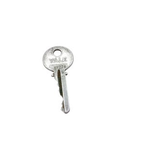 May include: A silver-colored Yale key with the text "YALE" and "8R278" stamped on the head. The key has a circular head with a hole and a grooved shaft. The key is designed for a lock.