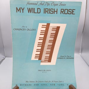 Puede incluir: Partitura musical titulada "MY WILD IRISH ROSE" de la serie Hammond And Pipe Organ. La portada es azul claro con el título en letras marrones. La música es de Chauncey Olcott, arreglada para órgano por Charles R. Cronham.