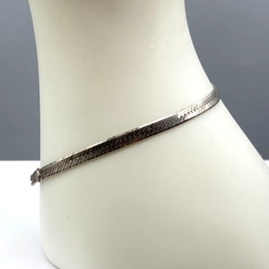 May include: A silver snake chain bracelet with a flat, textured design.