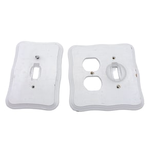 May include: Two white decorative light switch covers. One has a single switch opening, the other has two outlet openings and a switch opening. The covers have a wavy edge design and are slightly distressed.