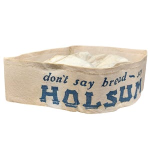May include: A vintage off-white fabric sailor-style hat featuring blue printed text that reads "don't say bread - say HOLSUM". The cap has a structured band and a soft, gathered crown, showcasing a classic nautical design with visible stitching.
