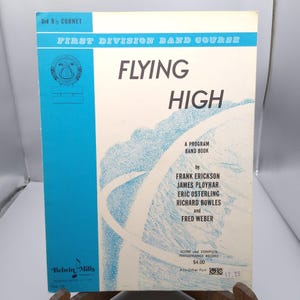 May include: A vintage music book titled "Flying High" with a blue and white cover. The cover features the text "Flying High" in large black letters, and the names of the authors. The book is a "First Division Band Course".
