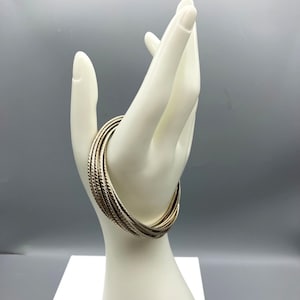 Può includere: Un set di braccialetti d'argento con finitura testurizzata. I braccialetti sono impilati uno sopra l'altro e sono indossati sul polso di un manichino.