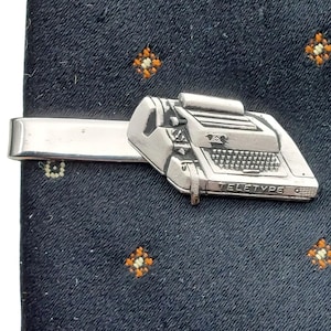 May include: Silver tie clip featuring a vintage typewriter with the word "Teletype" on the front.