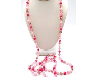 May include: A long, beaded necklace with a variety of pink and clear beads. The necklace is displayed on a white mannequin bust. The beads vary in size and shade, creating a gradient effect from light to dark pink.