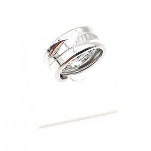 Puede incluir: Anillo de plata con un diseño de pluma. El anillo está hecho de dos bandas que se retuercen juntas. La banda inferior tiene las palabras "USA" y "STAIN" grabadas.