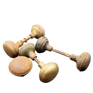 May include: A collection of antique door knobs with a weathered, aged appearance. The knobs are primarily brass and bronze, showing signs of rust and wear. The stems are made of metal. The knobs are arranged on a white background.
