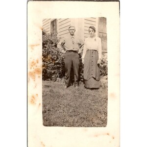 Cartão postal antigo AZO RPPC, casal de campo, homem e mulher em trajes elegantes, fora de casa