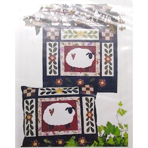 May include: A quilted wall hanging and pillow featuring a sheep design. The sheep are white with a heart-shaped detail, set against a floral background. The borders are adorned with floral and geometric patterns, with a dark blue background.