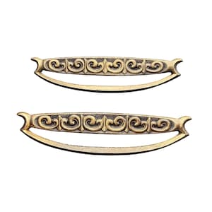 May include: Two antique brass-colored drawer pulls with a curved handle design. Each pull features an ornate, repeating scroll pattern across the top and curved ends. The pulls are set against a white background.