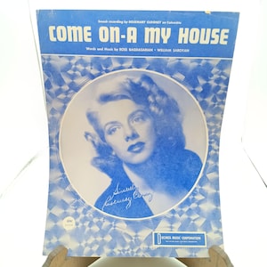 以下が含まれることがあります： ローズマリー・クルーニーの写真が載った、「Come On-A My House」という曲のヴィンテージ楽譜の表紙。表紙は青色で、中央に白い円形があります。曲名は大きく太字の青色の文字で書かれています。楽譜は販売中です。