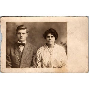 Antica cartolina postale RPPC dei primi anni del 1900, ritratto in tonalità seppia di una giovane coppia in abito formale, adatta per collezionisti o esposizione storica.