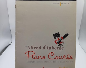 May include: Vintage "Alfred d'Auberge Piano Course" book. The cover is off-white with red and black text. The title is in a cursive font. A cartoon figure in a tuxedo plays a piano. The book is Book Three.