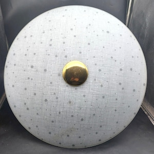 May include: A round, light gray ceiling light fixture with a gold-colored center button. The light has a speckled pattern and a textured surface. The fixture is designed for overhead lighting.
