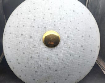 Può includere: Un apparecchio di illuminazione a soffitto rotondo grigio chiaro con un pulsante centrale dorato. La luce ha un motivo maculato e una superficie strutturata. Progettato per l'illuminazione dall'alto.