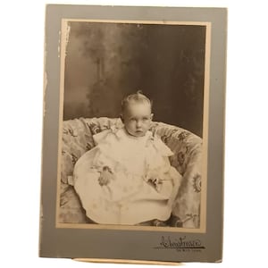 Fotografía antigua de un bebé en cartón, de finales del siglo XIX, de la época victoriana, en tono sepia, montada sobre cartón.