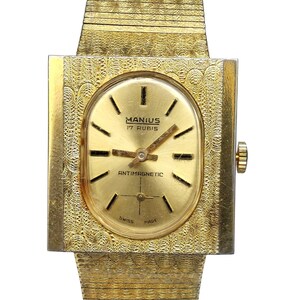 Puede incluir: Un reloj de pulsera dorado con una caja cuadrada y una esfera de forma ovalada. La esfera es dorada con marcas negras y el texto "MANIUS 17 RUBIS" y "ANTIMAGNETIC".