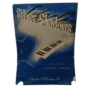 May include: A vintage sheet music cover for a piano solo titled "Silver Shadows" by Francis E. Aulbach. The cover features a stylized image of a piano keyboard with a blue and white background.
