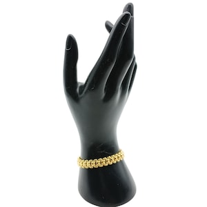 Puede incluir: Un brazalete de cadena dorada con un diseño tejido único.