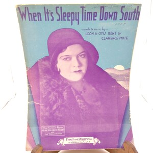Op de afbeelding: Vintage bladmuziekcover voor "When It's Sleepy Time Down South" met een portret van een vrouw met een hoed en een jas met bontkraag. De titel staat in blauw, met de namen van de songwriters en het jaar 1957.