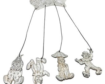 Può includere: Una carillon eolico color argento con un design stravagante di clown e mongolfiere. Il carillon ha quattro figure di clown appese sotto un pezzo superiore decorativo con dettagli di mongolfiere. I clown sono in varie pose.