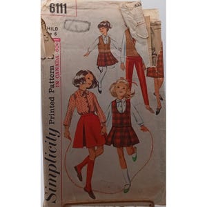 Può includere: Modello di cucito Simplicity vintage per un outfit per bambini. L'illustrazione mostra ragazze in vari outfit, tra cui gonne e camicette a quadri. La copertina del modello è invecchiata, con il numero 6111 visibile.